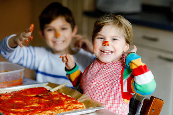 Dva sourozenci, malé děti, co doma dělají italskou pizzu. Roztomilé batole dívka a školák baví v domácí kuchyni, uvnitř. Bratr a sestra, rodina pomáhá a připravuje jídlo - Fotografie, Obrázek