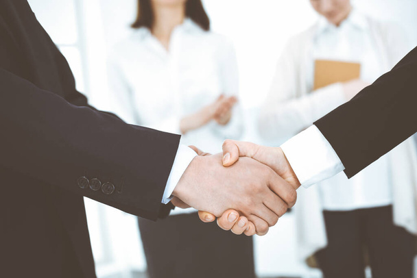 Businessman and woman shaking hands with colleagues at the background. Handshake at meeting in office. Concept of success in business - Фото, изображение
