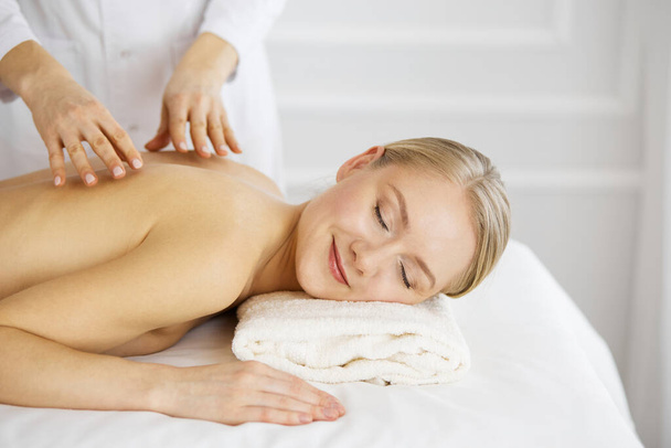 Beautiful caucasian woman enjoying back massage with closed eyes. Beauty and Spa salon concept - Foto, afbeelding