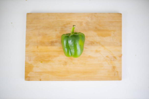 Green bell pepper on a cutting board above a white table - Фото, изображение