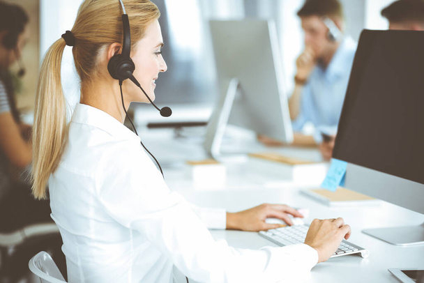 Blonde business woman using headset for communication and consulting people at customer service office. Call center. Group of operators at work - Fotoğraf, Görsel