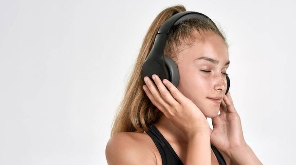 Portrait of cute sportive girl child wearing headphones, listening to music, standing with eyes closed while posing isolated over white background - Foto, Bild