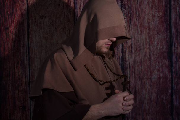 Ortaçağ keşişi kollarında tahta haçla gözleri kapalı dua ediyor. - Fotoğraf, Görsel