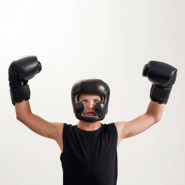 Disabled boy with Down syndrome wearing boxing gloves and helmet, looking at camera, raising his arms, feeling strong while posing isolated over white background - Φωτογραφία, εικόνα