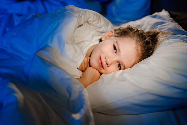 a cute girl is lying in bed and smiling. calm and healthy childrens sleep - Fotoğraf, Görsel