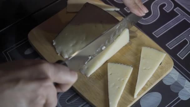 Το γυναικείο χέρι κόβει τυρί με ένα πολύ μεγάλο κοφτερό μαχαίρι σε μια ξύλινη σανίδα σε μια κουζίνα με έναν τοίχο βαμμένο μωβ. Τραβήχτηκε από την αρχή. Τρόφιμα - Πλάνα, βίντεο