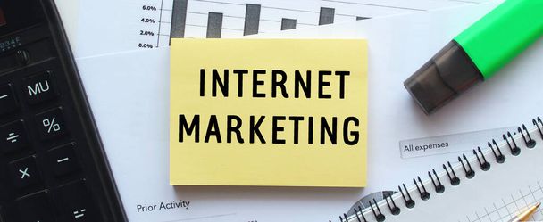 Text INTERNET MARKETING on the page of a notepad lying on financial charts on the office desk. Near the calculator. Business concept. - Φωτογραφία, εικόνα