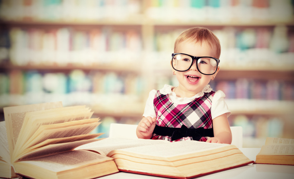 Bébé fille drôle dans des lunettes de lecture d'un livre dans une bibliothèque
 - Photo, image