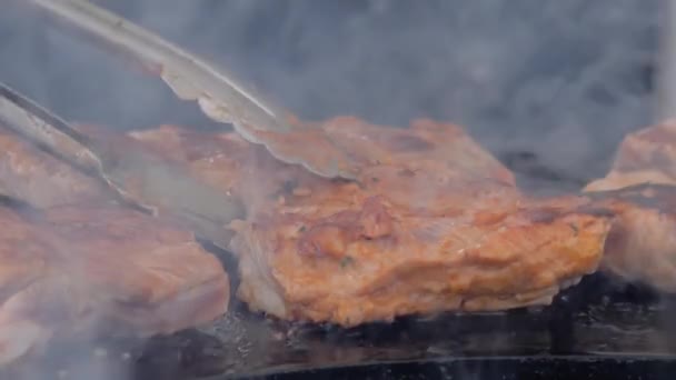 Zwolnij tempo: szef kuchni z szczypcami grillujący steki mięsne na kozieradce - zbliżenie - Materiał filmowy, wideo