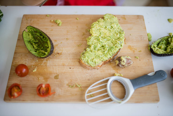 Female hands spreading avocado on a slice of bread above cutting board - Photo, Image