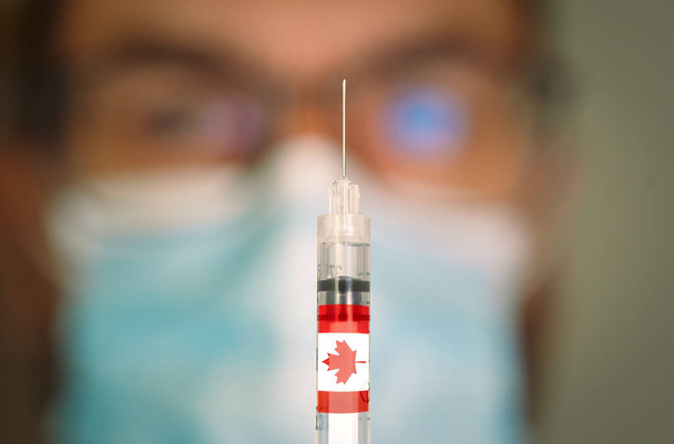 Close-up da seringa hipodérmica com a bandeira do Canadá e médico desfocado em segundo plano. - Foto, Imagem
