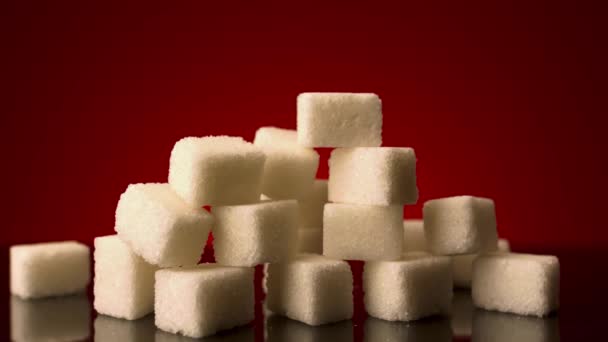 Közel sok cukorkocka áll egymás tetején, vörös háttérrel elszigetelve. Készletfelvétel. A cukorka, édességek és élelmiszerek fogalma.  - Felvétel, videó
