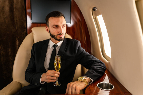 Handsome businessman wearing elegant suit  flying on exclusive private jet - Successful entrepreneur sitting in exclusive business class on airplane, concepts about business and trasportation - Foto, Imagen