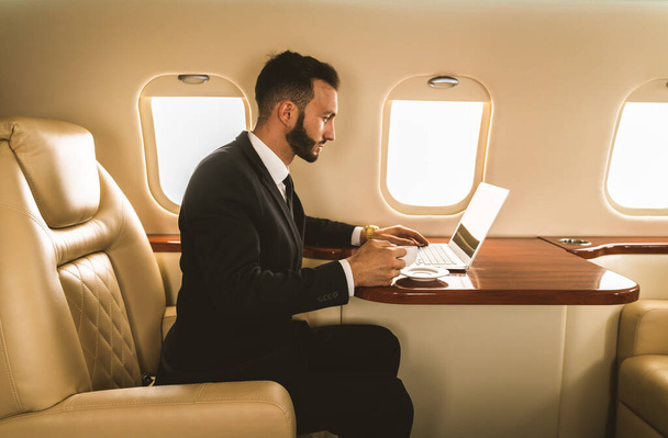 Handsome businessman wearing elegant suit  flying on exclusive private jet - Successful entrepreneur sitting in exclusive business class on airplane, concepts about business and trasportation - Fotografie, Obrázek