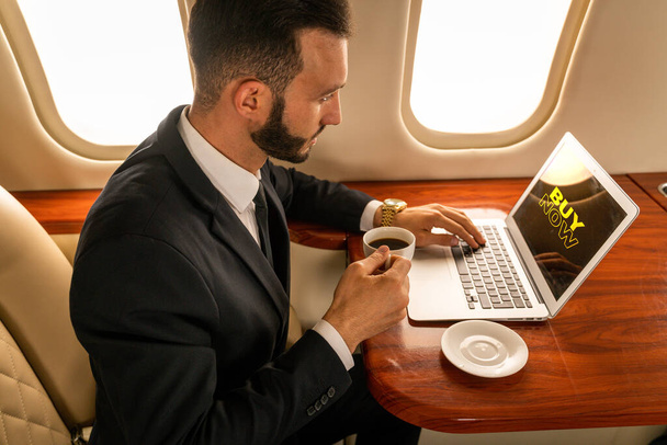 Όμορφος επιχειρηματίας φορώντας κομψό κοστούμι που φέρουν με αποκλειστικό ιδιωτικό τζετ - Επιτυχημένος επιχειρηματίας κάθεται στην αποκλειστική επιχειρηματική θέση στο αεροπλάνο, έννοιες σχετικά με τις επιχειρήσεις και trasportation - Φωτογραφία, εικόνα