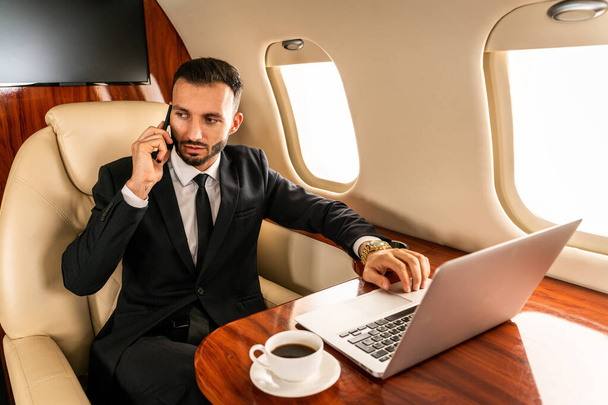 Handsome businessman wearing elegant suit  flying on exclusive private jet - Successful entrepreneur sitting in exclusive business class on airplane, concepts about business and trasportation - Foto, imagen