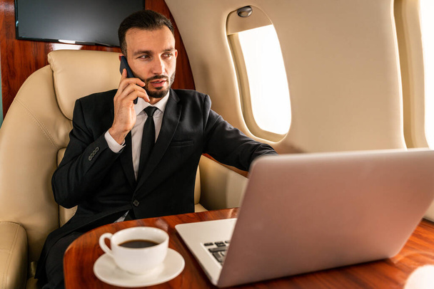Handsome businessman wearing elegant suit  flying on exclusive private jet - Successful entrepreneur sitting in exclusive business class on airplane, concepts about business and trasportation - Foto, afbeelding