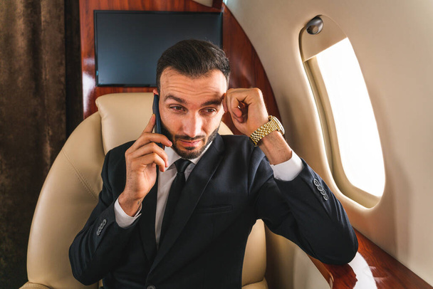 Handsome businessman wearing elegant suit  flying on exclusive private jet - Successful entrepreneur sitting in exclusive business class on airplane, concepts about business and trasportation - Foto, Imagen