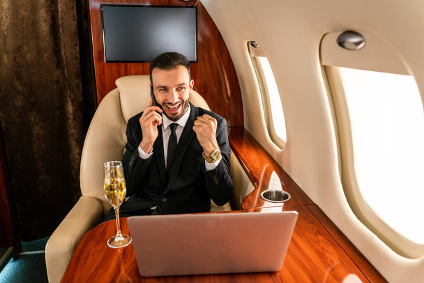 Handsome businessman wearing elegant suit  flying on exclusive private jet - Successful entrepreneur sitting in exclusive business class on airplane, concepts about business and trasportation - Valokuva, kuva
