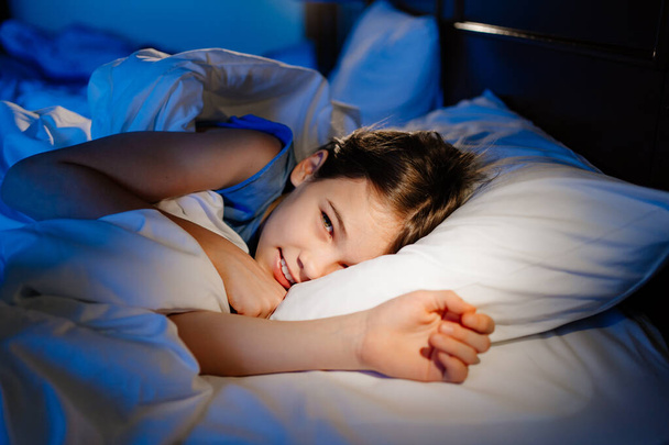 a girl is lying in bed and smiling. calm and healthy childrens sleep - Φωτογραφία, εικόνα