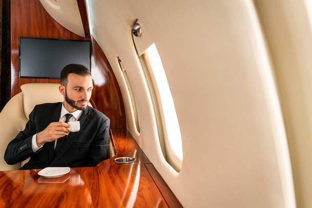 Handsome businessman wearing elegant suit  flying on exclusive private jet - Successful entrepreneur sitting in exclusive business class on airplane, concepts about business and trasportation - Фото, изображение