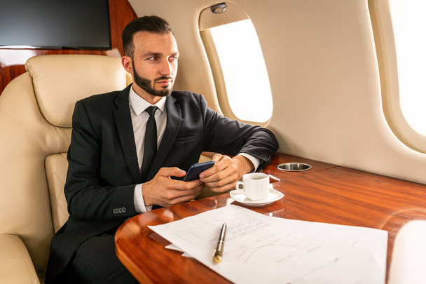 Bonito empresário vestindo terno elegante voando em jato privado exclusivo - Empresário bem sucedido sentado em classe executiva exclusiva em avião, conceitos sobre negócios e trasportação - Foto, Imagem
