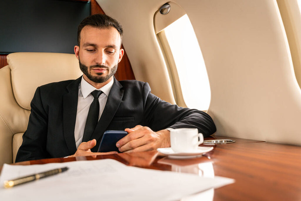 Handsome businessman wearing elegant suit  flying on exclusive private jet - Successful entrepreneur sitting in exclusive business class on airplane, concepts about business and trasportation - Фото, зображення