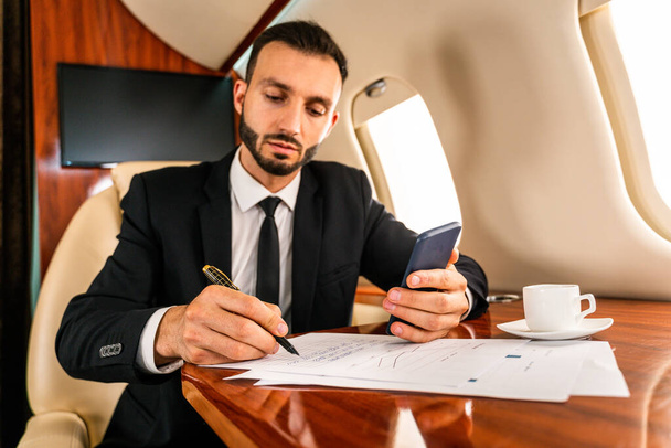 Handsome businessman wearing elegant suit  flying on exclusive private jet - Successful entrepreneur sitting in exclusive business class on airplane, concepts about business and trasportation - Photo, image