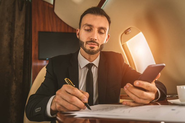 Jóképű üzletember elegáns öltönyt visel repülő exkluzív magángép - Sikeres vállalkozó ül exkluzív üzleti osztály repülőn, fogalmak üzleti és közlekedési - Fotó, kép