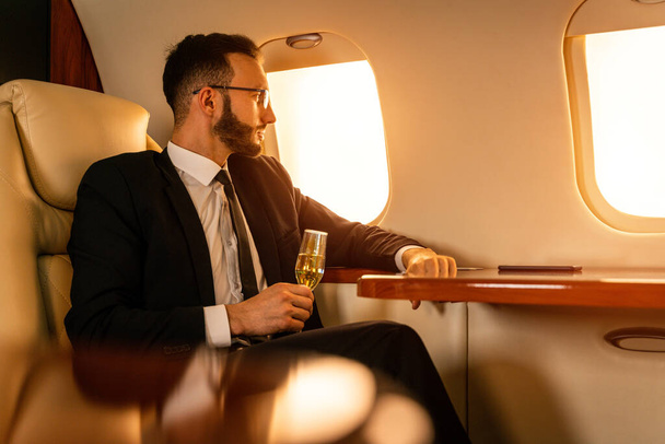 Handsome businessman wearing elegant suit  flying on exclusive private jet - Successful entrepreneur sitting in exclusive business class on airplane, concepts about business and trasportation - Φωτογραφία, εικόνα