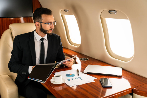 Handsome businessman wearing elegant suit  flying on exclusive private jet - Successful entrepreneur sitting in exclusive business class on airplane, concepts about business and trasportation - Foto, immagini