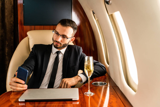 Handsome businessman wearing elegant suit  flying on exclusive private jet - Successful entrepreneur sitting in exclusive business class on airplane, concepts about business and trasportation - Fotó, kép