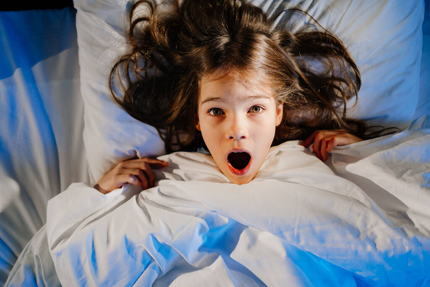 A frightened girl in bed in her room, sees a nightmare. childs fear - Photo, image