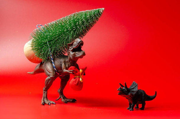Dinosaur toy with fir tree on red background. Happy new year - Φωτογραφία, εικόνα
