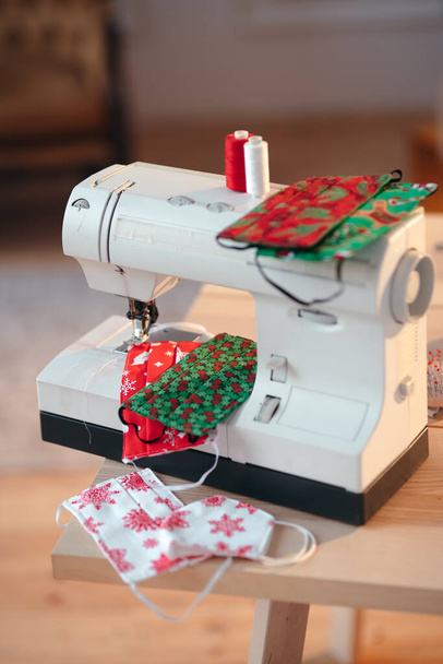 Workplace of a tailor working from home during Christmas. Sewing Christmas patterned face masks on a brand new sewing machine - Valokuva, kuva