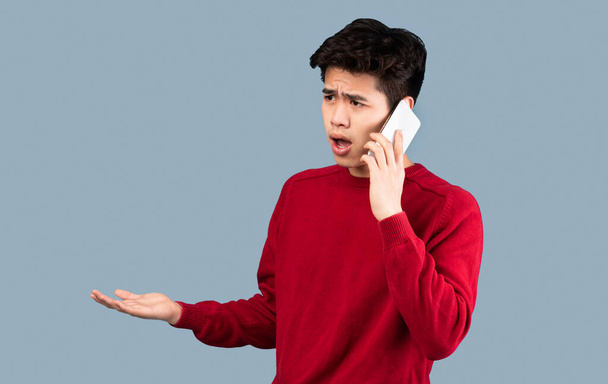 confuso asiatico uomo parlando su smartphone a studio - Foto, immagini