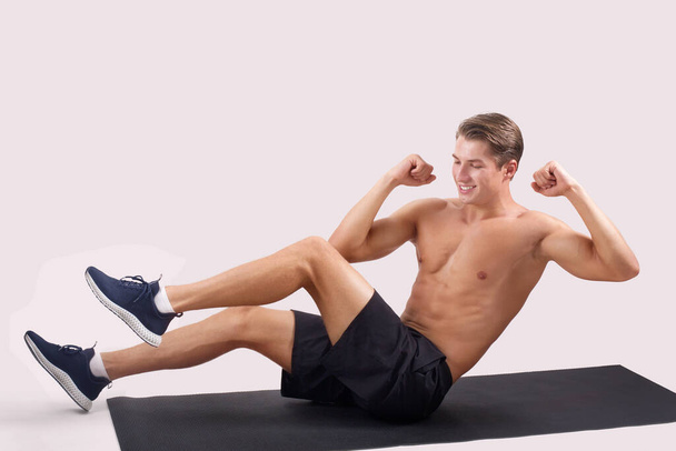 Strong young guy exercising on sports mat, working on abs muscles over light studio background, copy space - Photo, image
