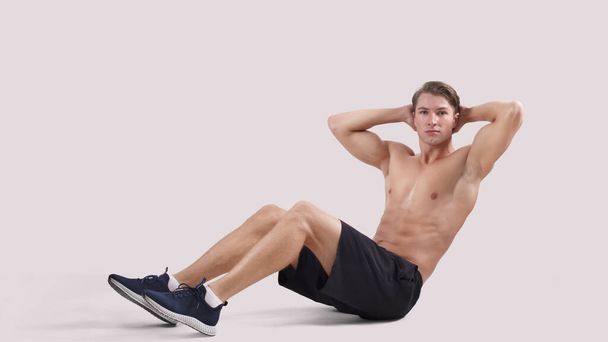 Athletic young man with sexy body doing abs exercises over light studio background, panorama - Fotografie, Obrázek