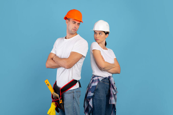 Νεαρό ζευγάρι διαφωνεί κατά τη διάρκεια επιδιόρθωσης σπίτι στέκεται προσβεβλημένος πάνω από μπλε φόντο - Φωτογραφία, εικόνα