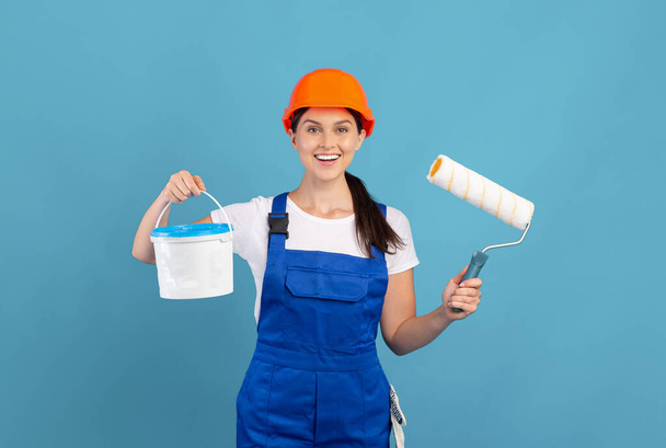 Šťastný mladý malíř dáma nosit kombinézy držení kbelík a vybavení pro malování - Fotografie, Obrázek