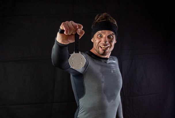 Красавчик в спортивной одежде безумно радуется полученной серебряной медали в студии на черном фоне - Фото, изображение