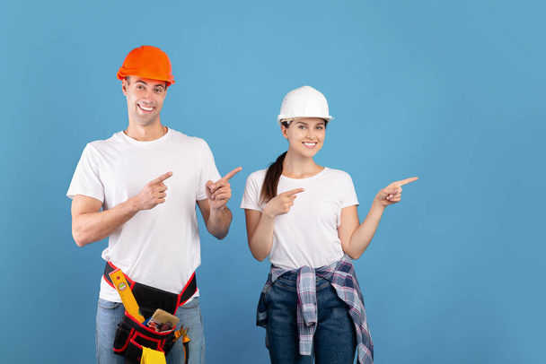 Couple souriant de travailleurs manuels portant des vêtements décontractés et des chapeaux durs protecteurs pointant de côté - Photo, image