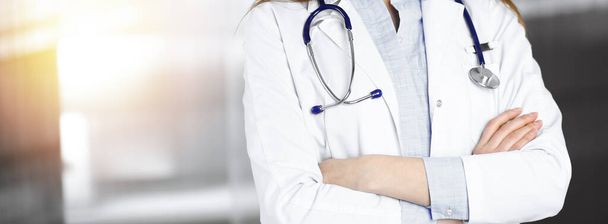 Neznámá mladá doktorka stojí se zkříženýma rukama na slunné klinice. Medicína koncepce během Koronavirus pandemie. Covid-2019 - Fotografie, Obrázek