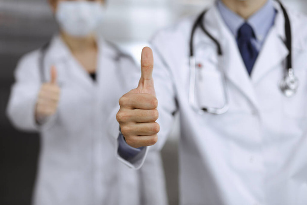 Unknown man-doctor and woman standing straight as a team and showing Ok sign with thumbs up in modern clinic. Medicine concept during Coronavirus pandemic. Covid 2019 - Фото, зображення