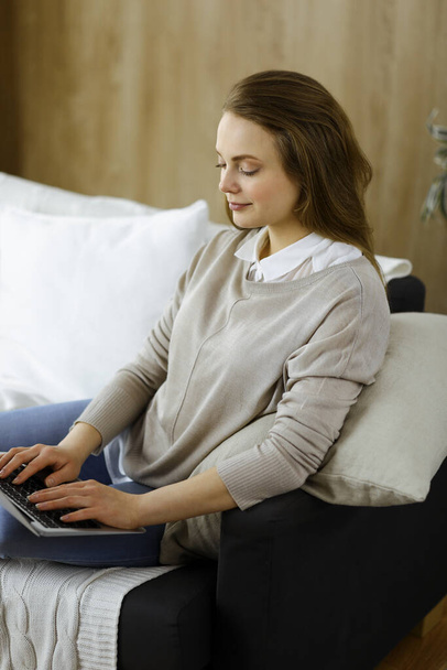 Geschäftsfrau, die am Laptop arbeitet, sitzt während der Covid-19-Quarantäne im gemütlichen Wohnzimmer. Während der Coronavirus-Pandemie zu Hause bleiben - Foto, Bild