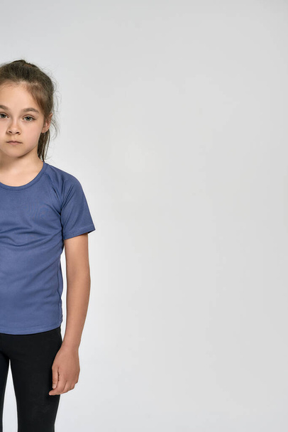 Cropped shot of little sportive girl child in sportswear looking at camera, while standing isolated over white background - 写真・画像