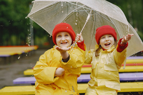 Funny kids in rain boots playing in a rainy park - Photo, image