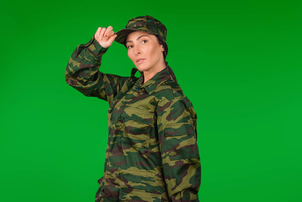 Serious woman in military uniform posing and looking at the camera on green background, space for advertisment. High quality photo - Foto, imagen