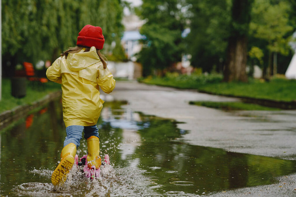 Lustige Kinder in Regenstiefeln spielen mit einem Papierschiff an einer Pfütze - Foto, Bild