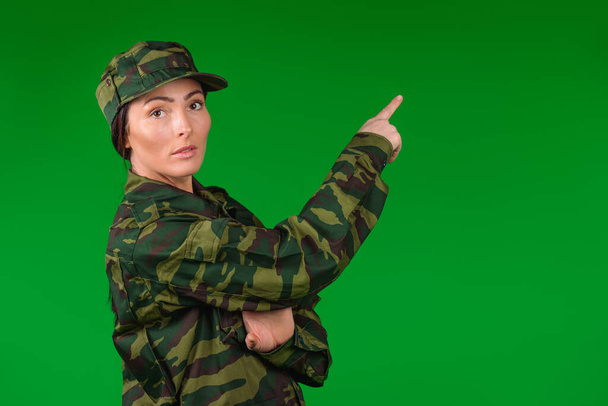Woman in military uniform looks at the camera and points index finger to the top. Green background. High quality photo - Photo, Image